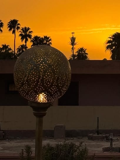 A pierced brass globe lamp against an orange sunset sky.